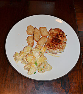 A top view of a plate with a pork chop, a handful of cauliflower tots, and a spoonful of Cheddar Ranch Potatoes.