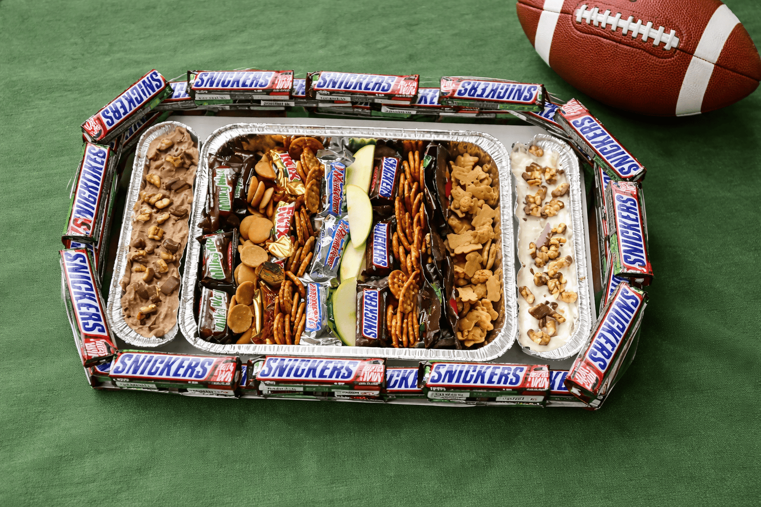 A snack stadium made with Snickers bars and dippers with a football behind the stadium.
