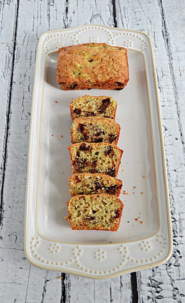 A mini chocolate chip zucchini loaf with one who loaf and one loaf sliced on a platter.
