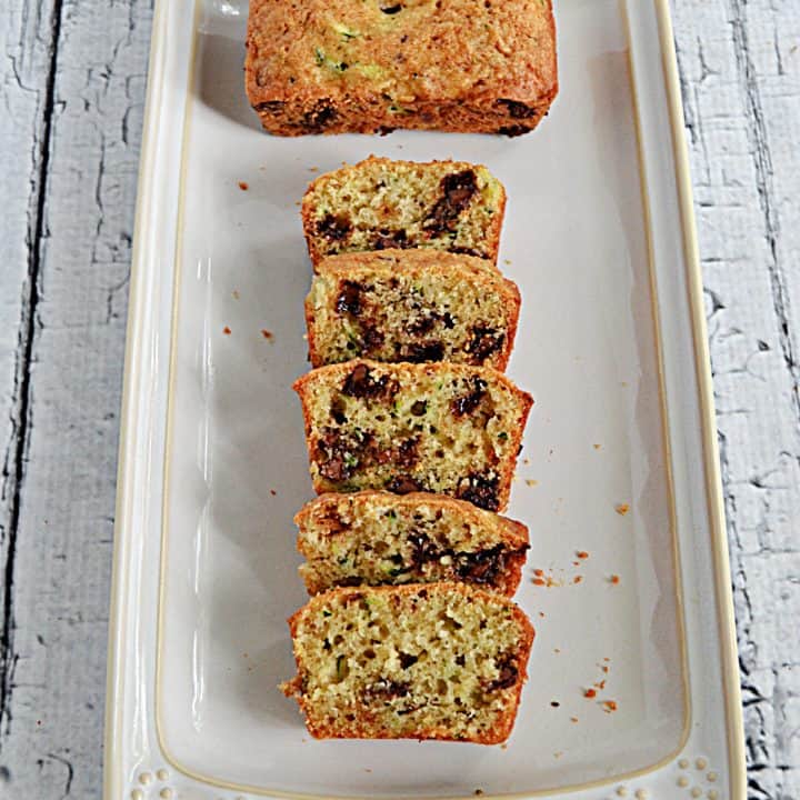 A mini chocolate chip zucchini loaf with one who loaf and one loaf sliced on a platter.