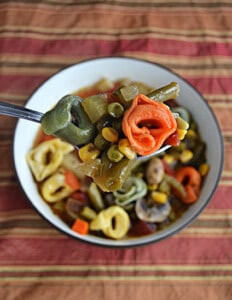 A bowl of tortellini vegetable soup with a spoonful lifted up out of the bbowl.