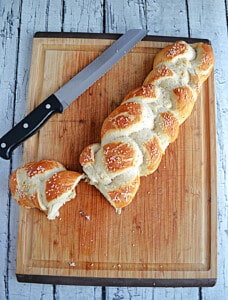 A loaf of Vegan Hot Pretzel Challah Bread with a slice cut off the end and the knife on the cutting board.