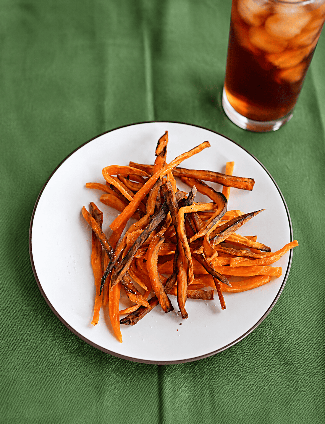 A plate of sweet potato fries with a glass of iced tea behind it.