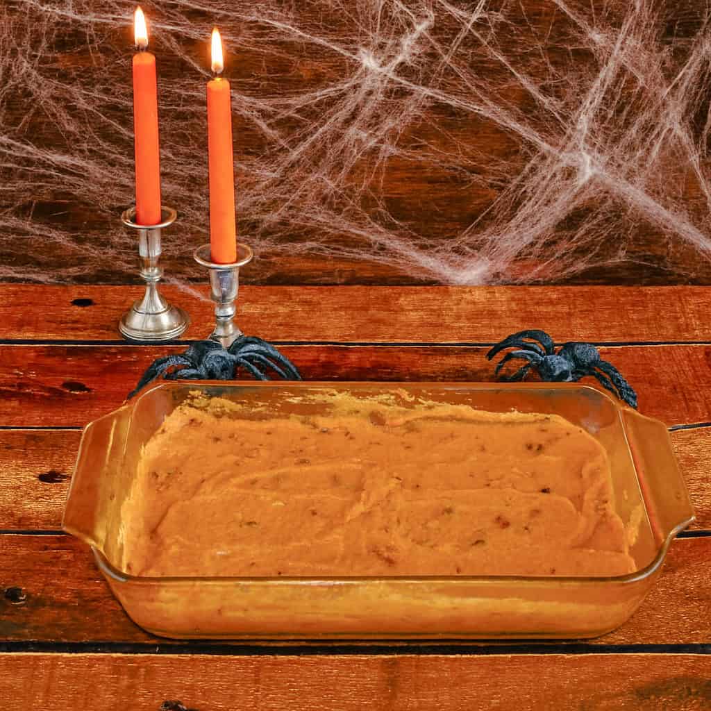 A pan of pumpkin dip with two orange candles and spiderwebs in the background.