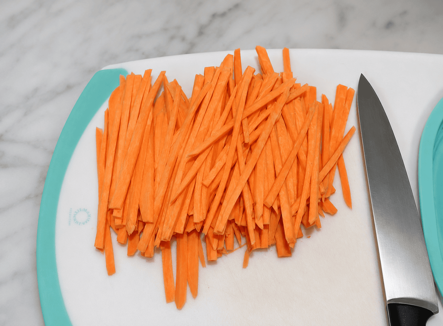 A cutting board with sweet potato sticks on it and a butcher knife.