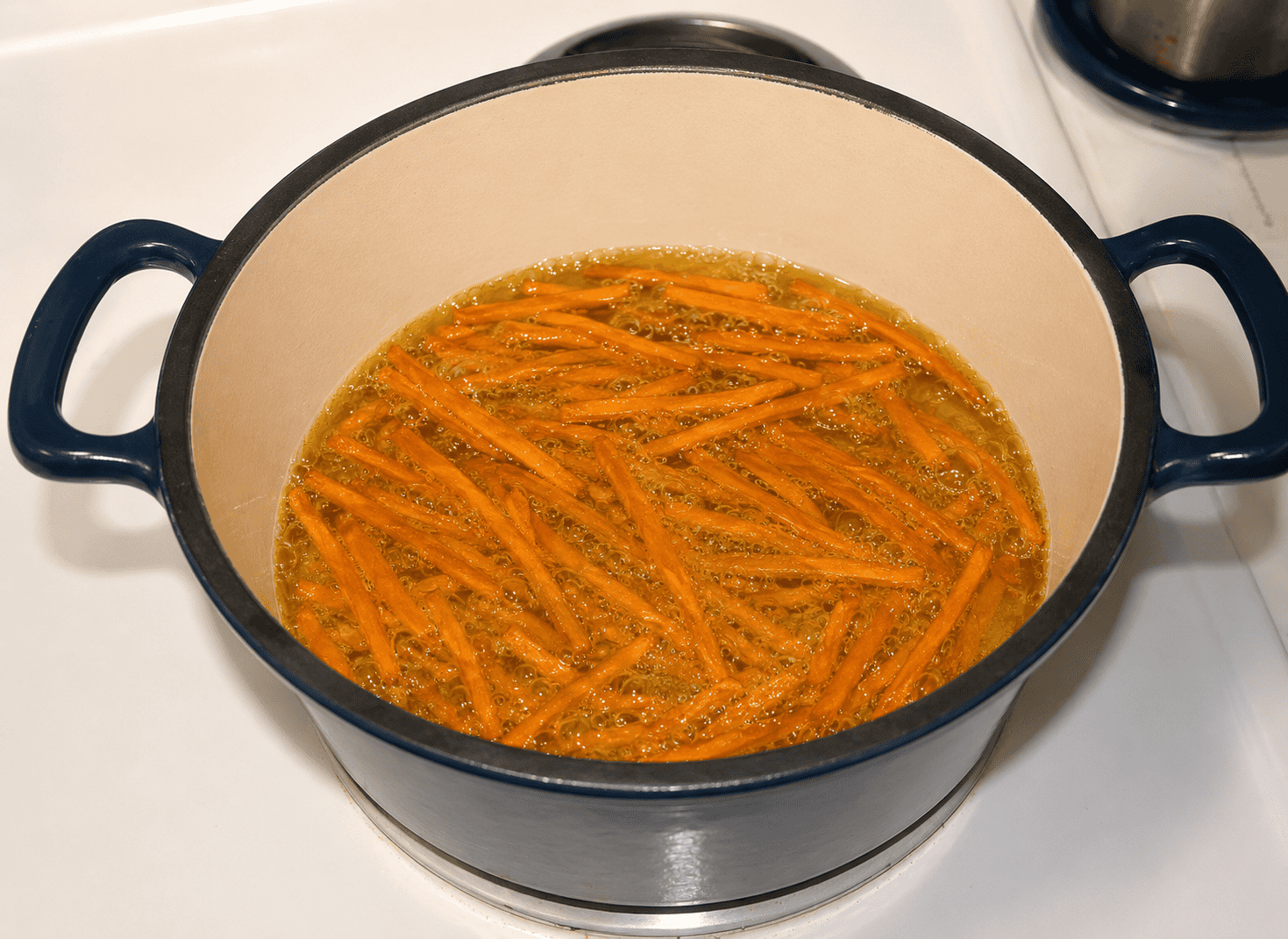 A pot of oil with sweet potato fries in it.