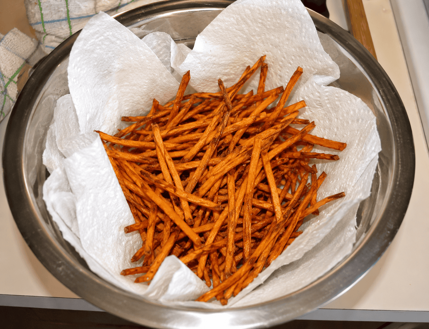 A colander with paper towels lining it and sweet potato fries in it.