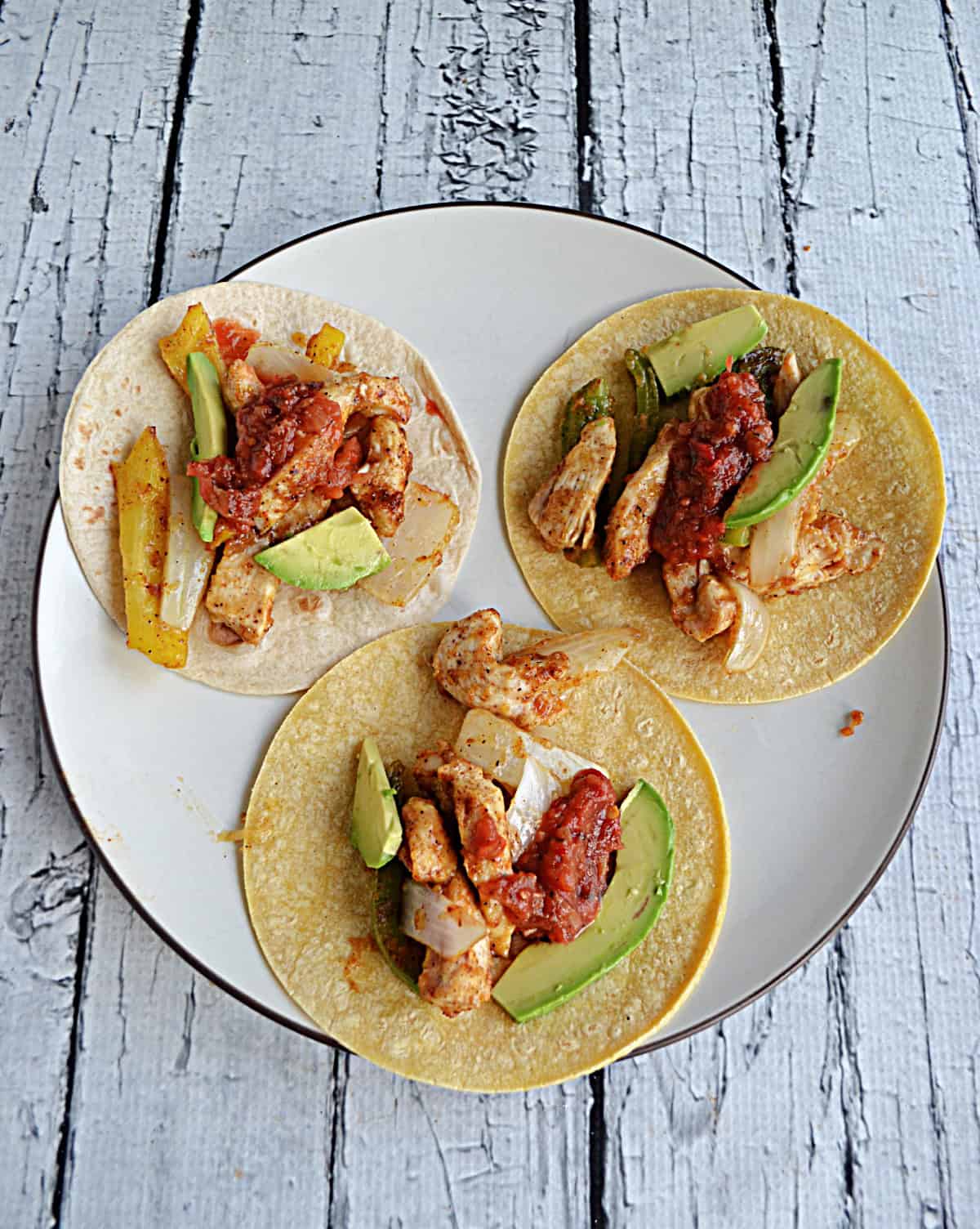 A plate with 3 tortillas topped with chicken, peppers, and onions.