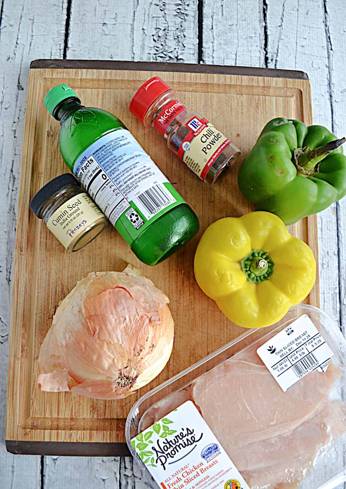 A cutting board with chicken, peppers, onions, and spices on it.