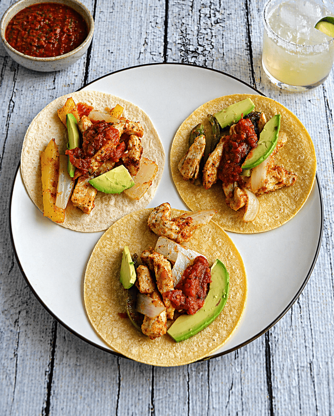 A plate of chicken fajitas with a margarita behind the plate.