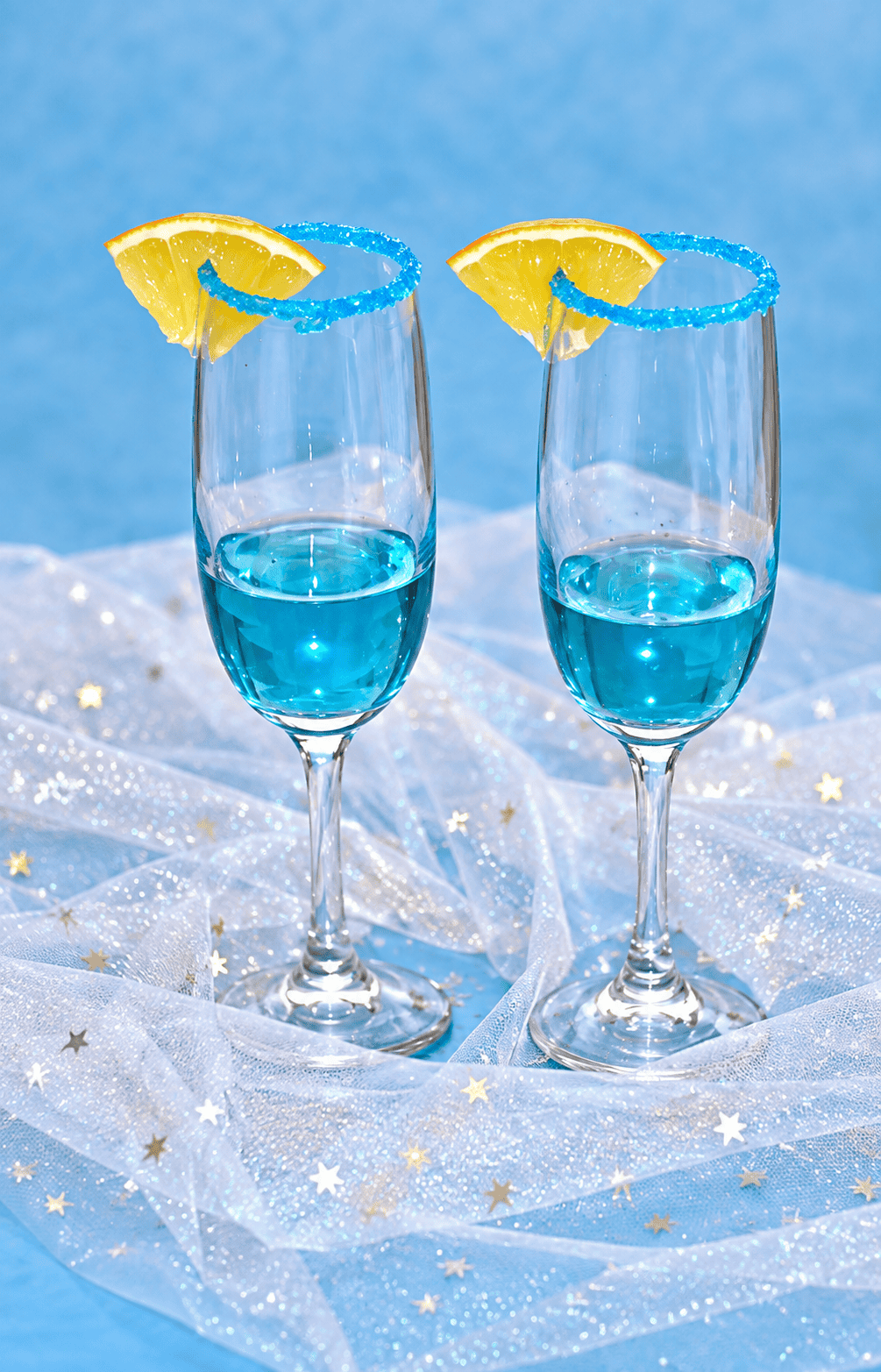 Two champagne glasses with blue liquid and an orange slice on the rim.