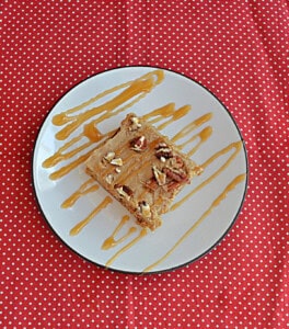 A plate drizzled with caramel with a blondie topped with pecans.