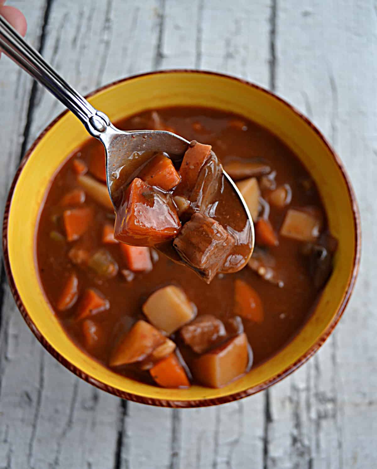 A spoon with a bite of stew on it and a bowl of stew underneath it.