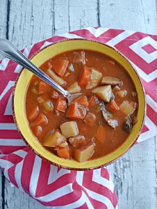 A bowl of beef stew with a spoon in it.