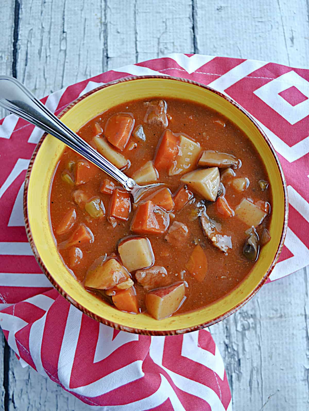 A bowl of beef stew with a spoon in it.