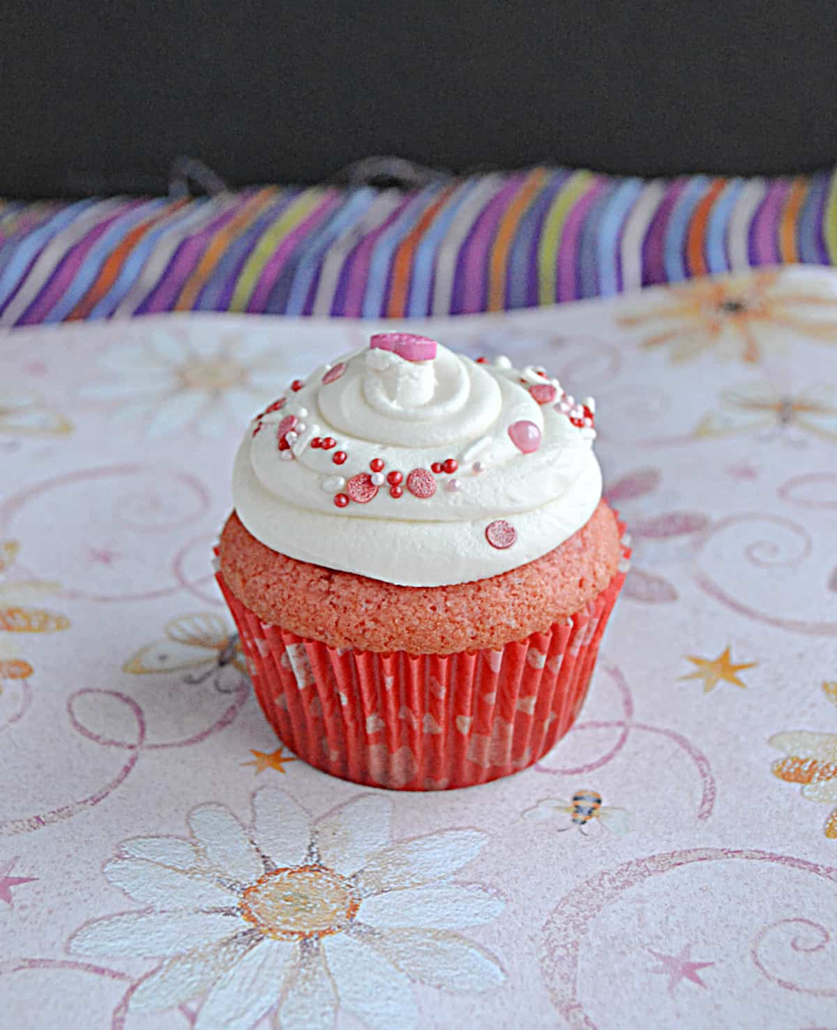 A pink velvet cupcake with white frosting on top.
