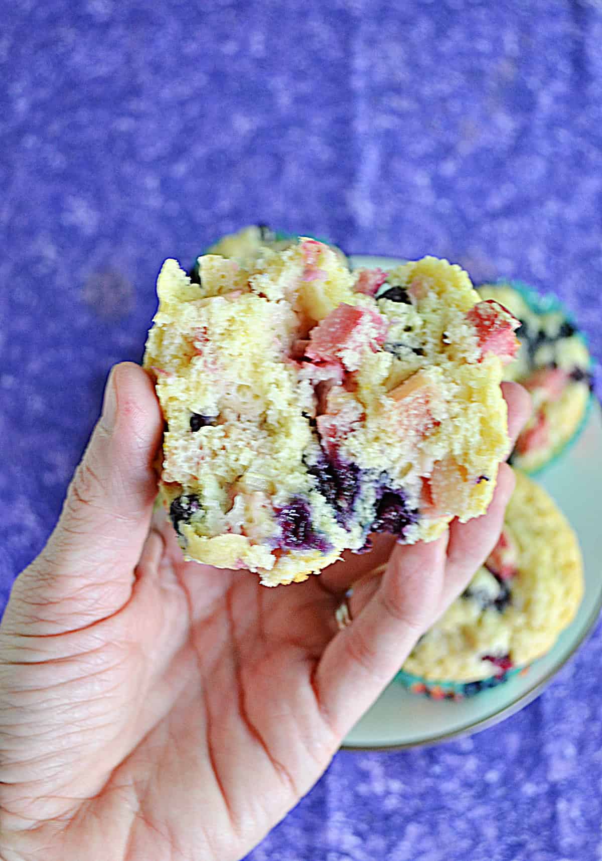 A hand holding a muffin broken in half.