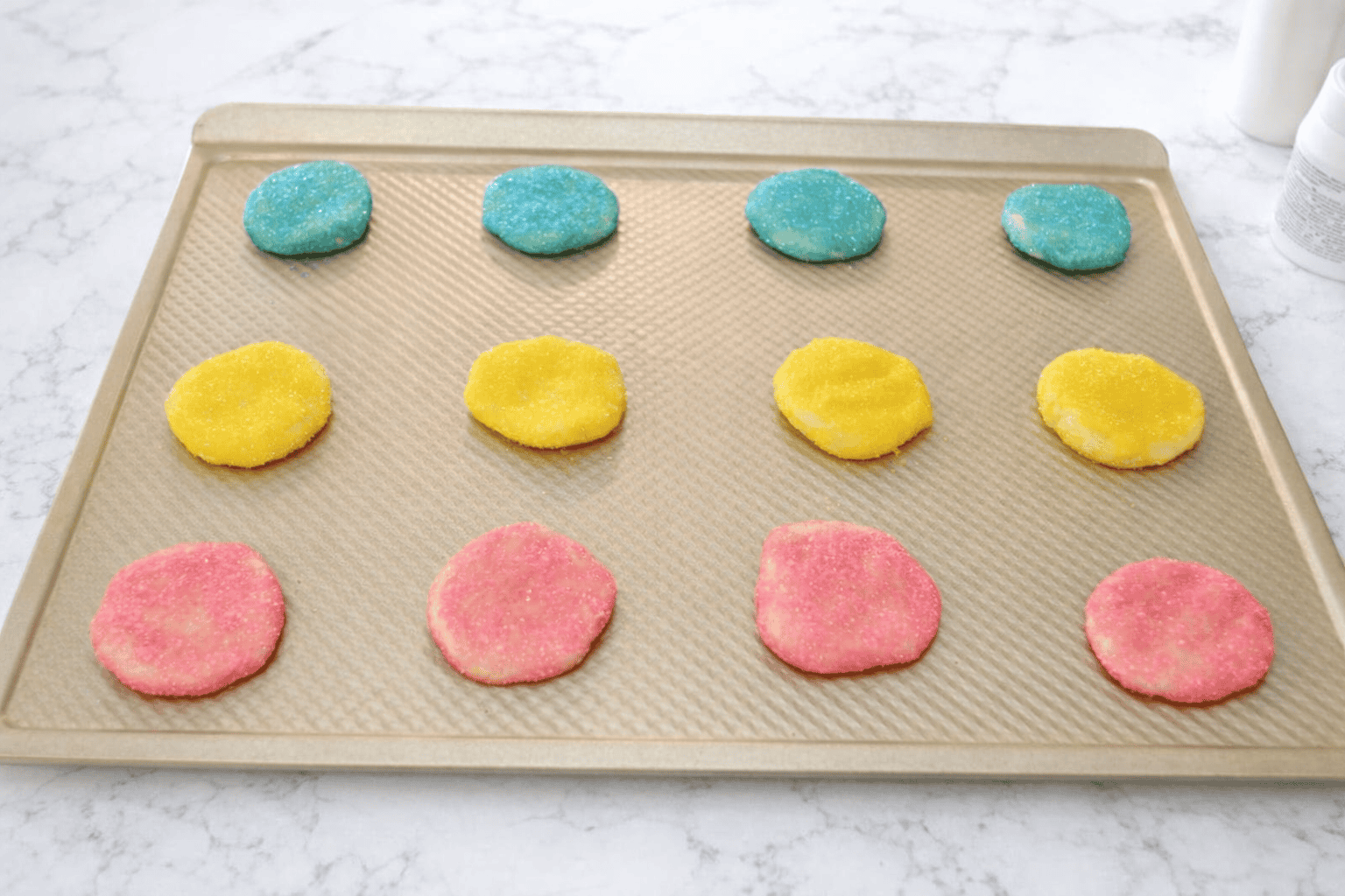 Cookies rolled in pastel sugar on a baking sheet.
