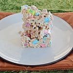 A plate stacked with Lucky Charms Treats on a gold background.