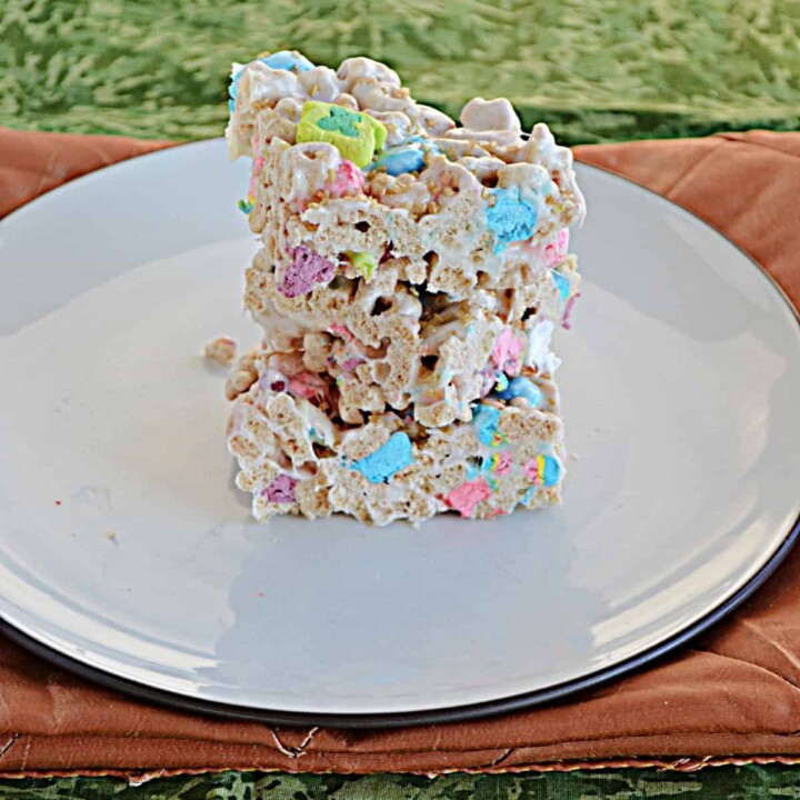 A plate stacked with Lucky Charms Treats on a gold background.