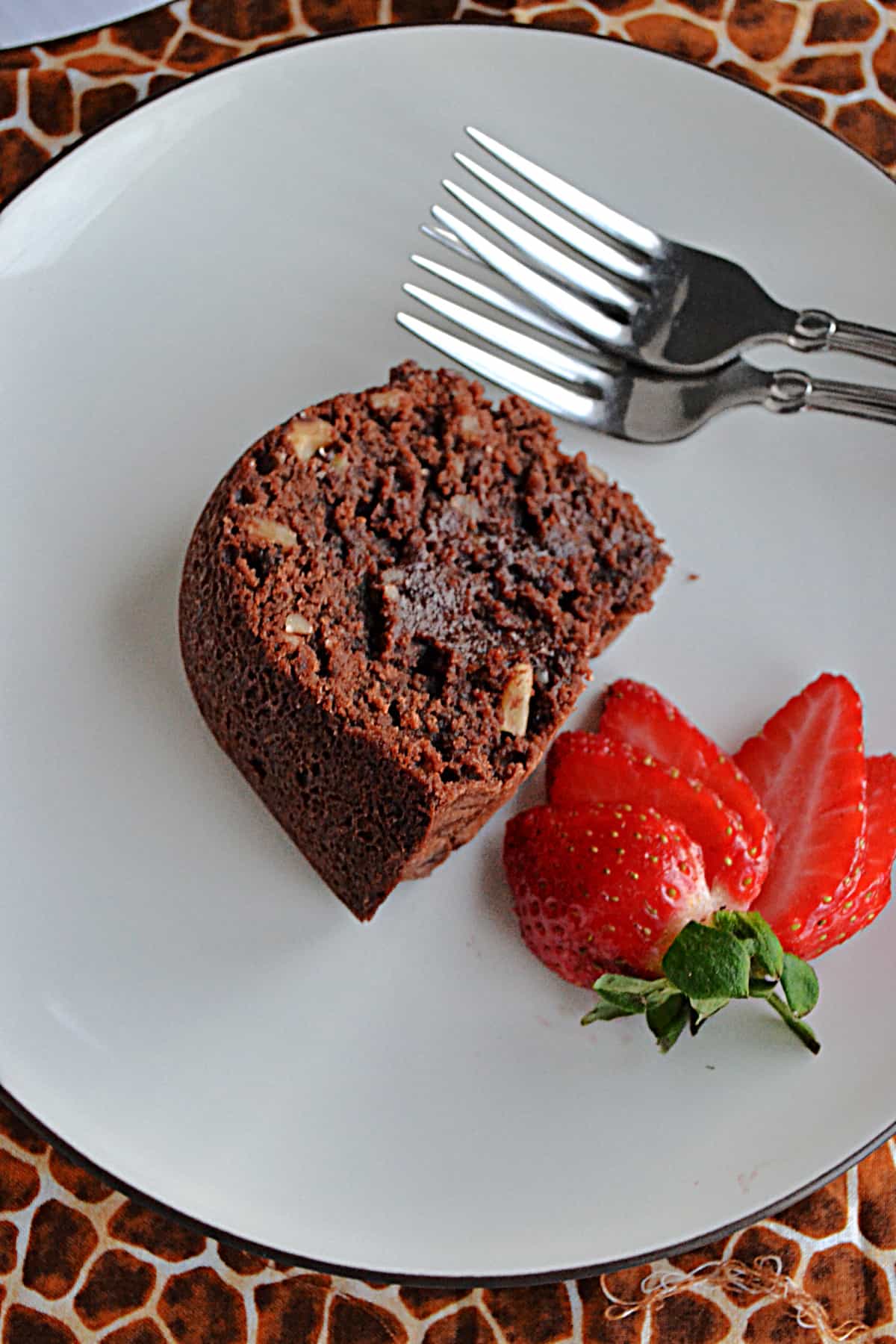 A close up of a slice of Tunnel of Fudge cake with a strawberry next to it.