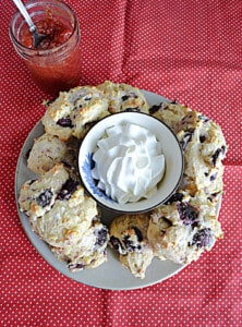 A plate of scones with whipped cream in the middle and cherry preserves on the side.