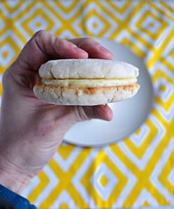 A hand holding a lemon sandwich cookie.