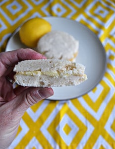 A hand holding a lemon sandwich cookie with a bite out of it.