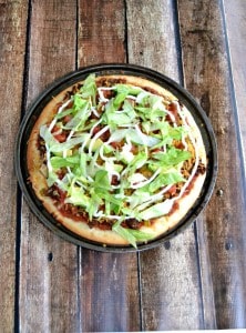 Delicious Taco Pizza starts with Sabra Salsa then is piled high with refried beans, seasoned ground beef, cheese, lettuce, and other toppings.