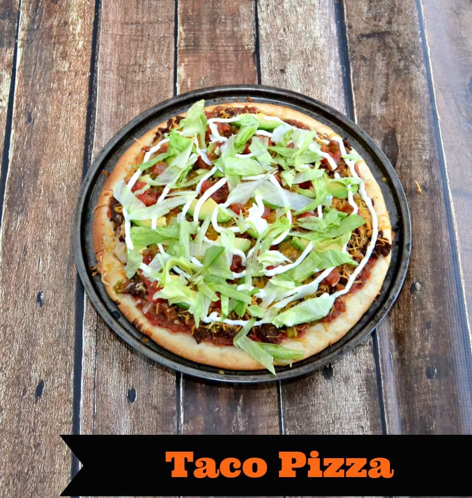Tasty Taco Pizza layered with your favorite taco topping like seasoned ground beef, cheese, refried beans, lettuce, sour cream, and more!