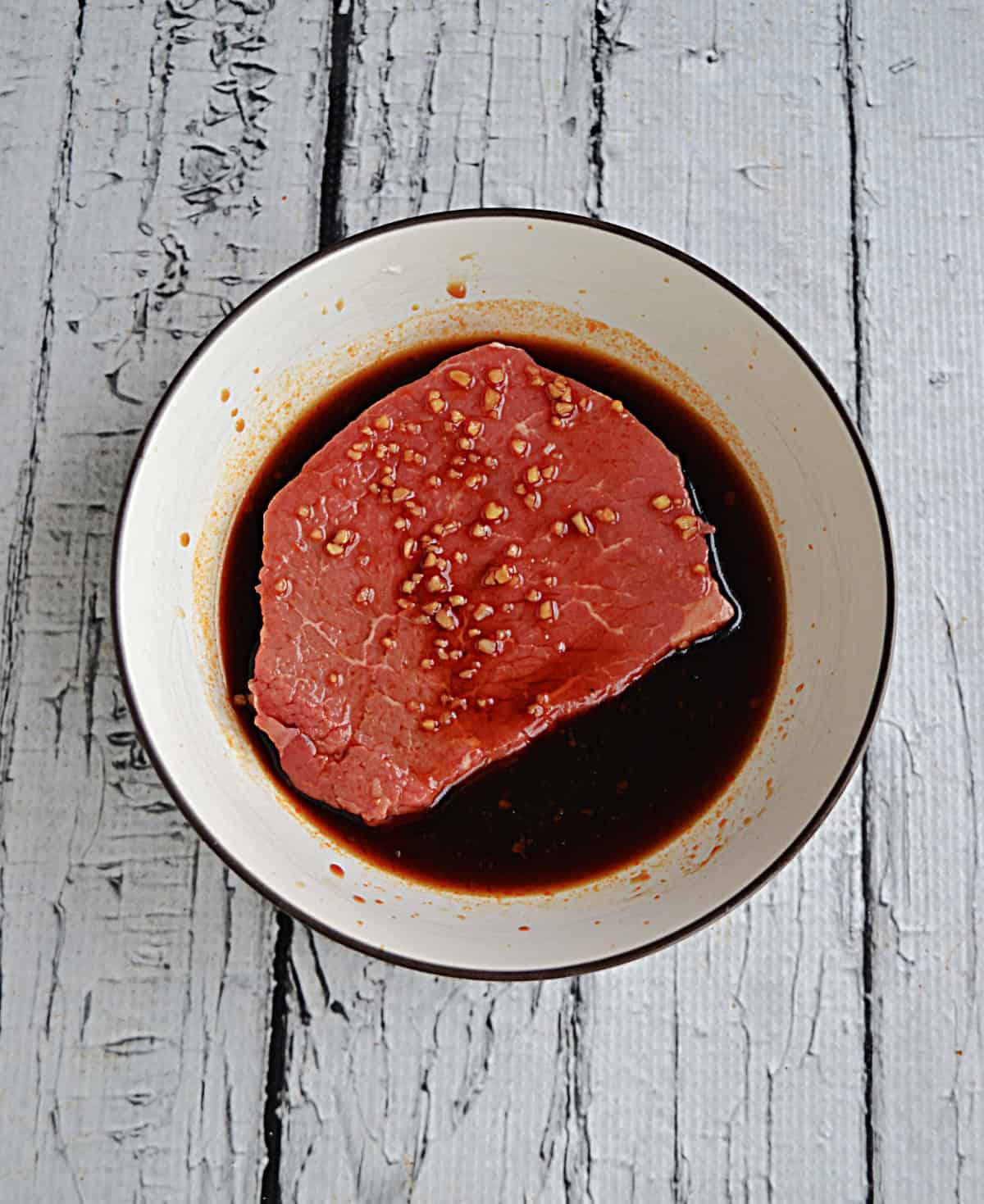 A bowl of marinade with a steak in it.