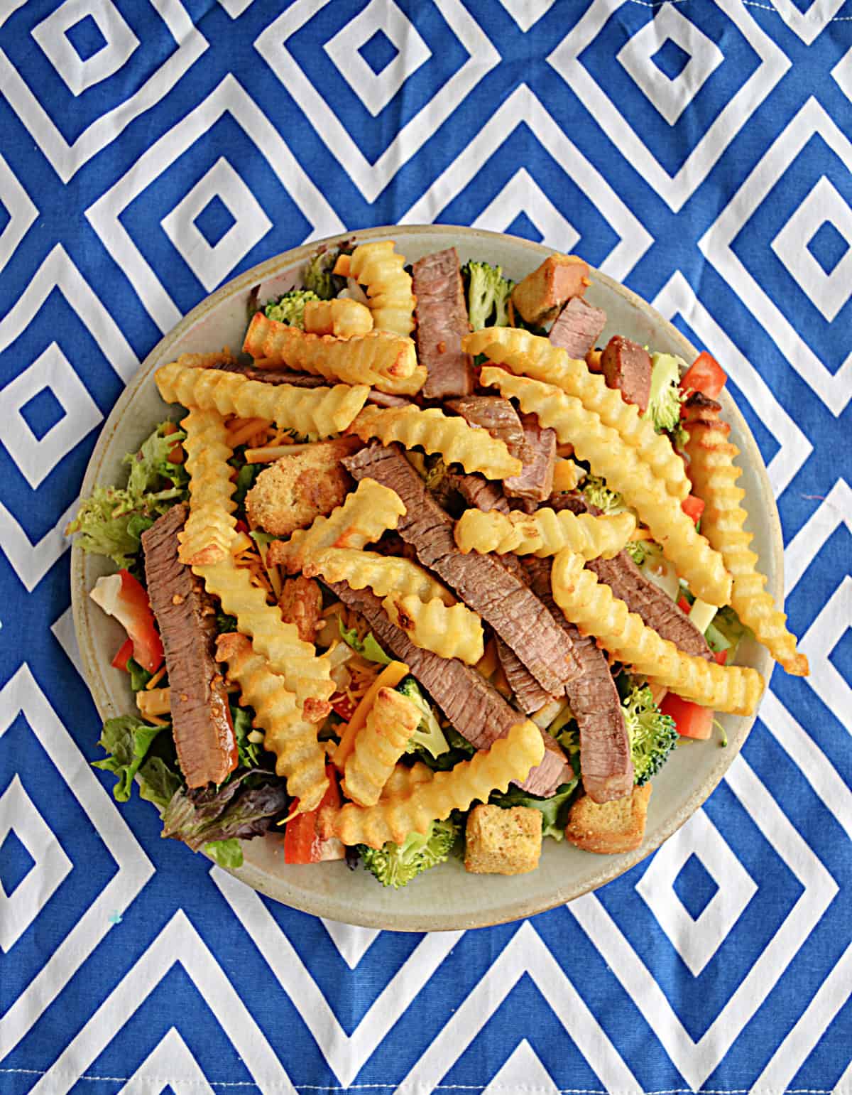 A plate of salad with steak and fries on top.