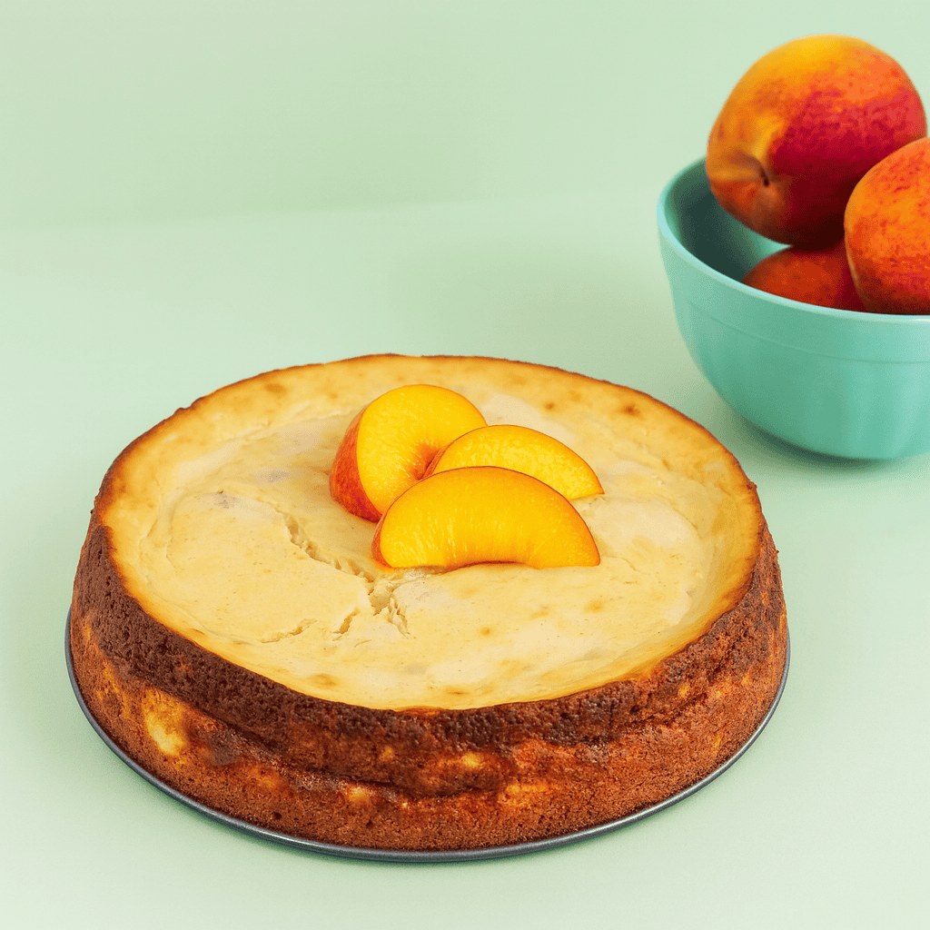 A cheesecake with sliced peaches on top of it and a bowl of peaches.