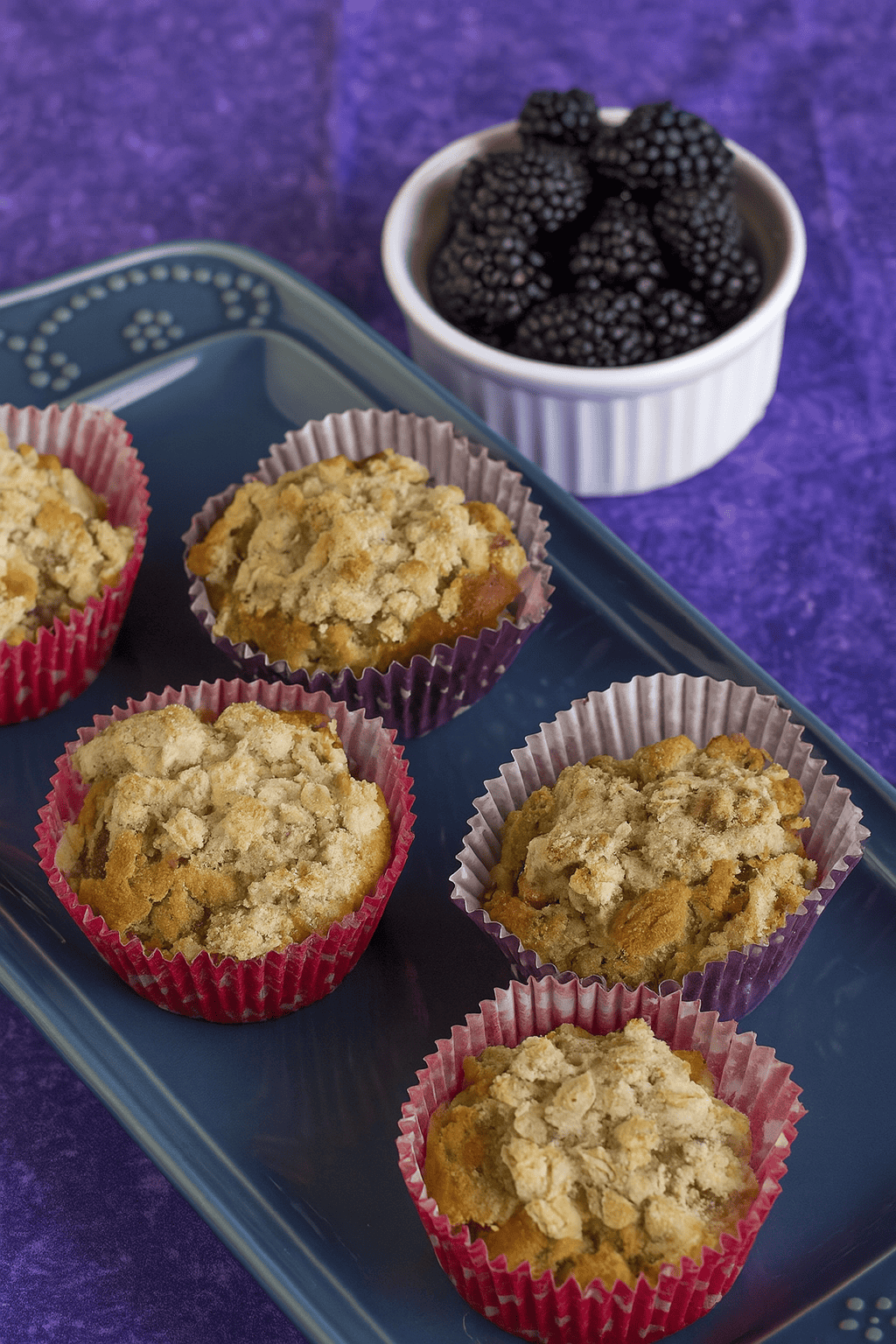 A close up of a platter of muffins with a bowl of blackberries in the background.
