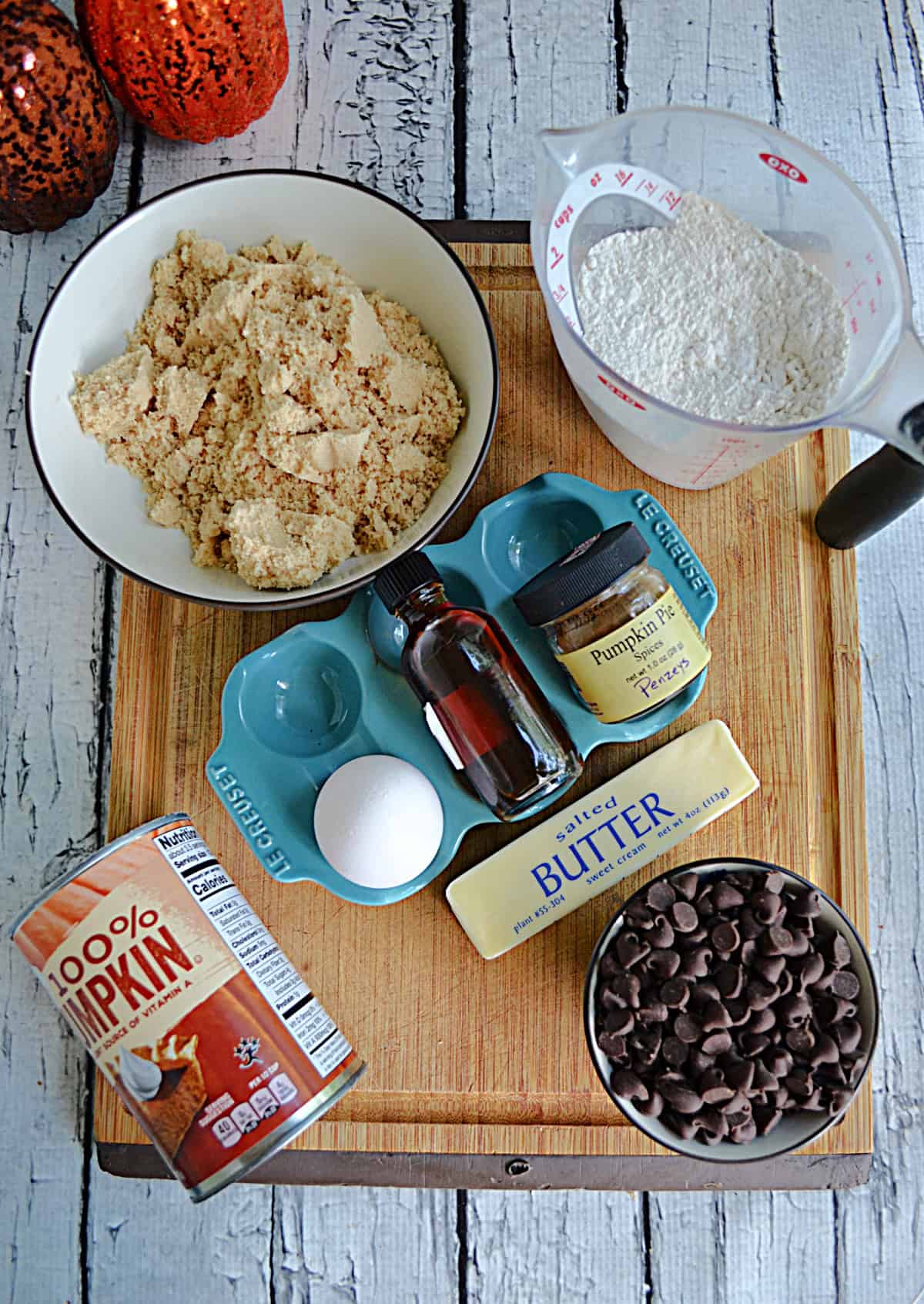 A cutting board with brown sugar, flour, butter, egg, pumpkin, and flour on it.