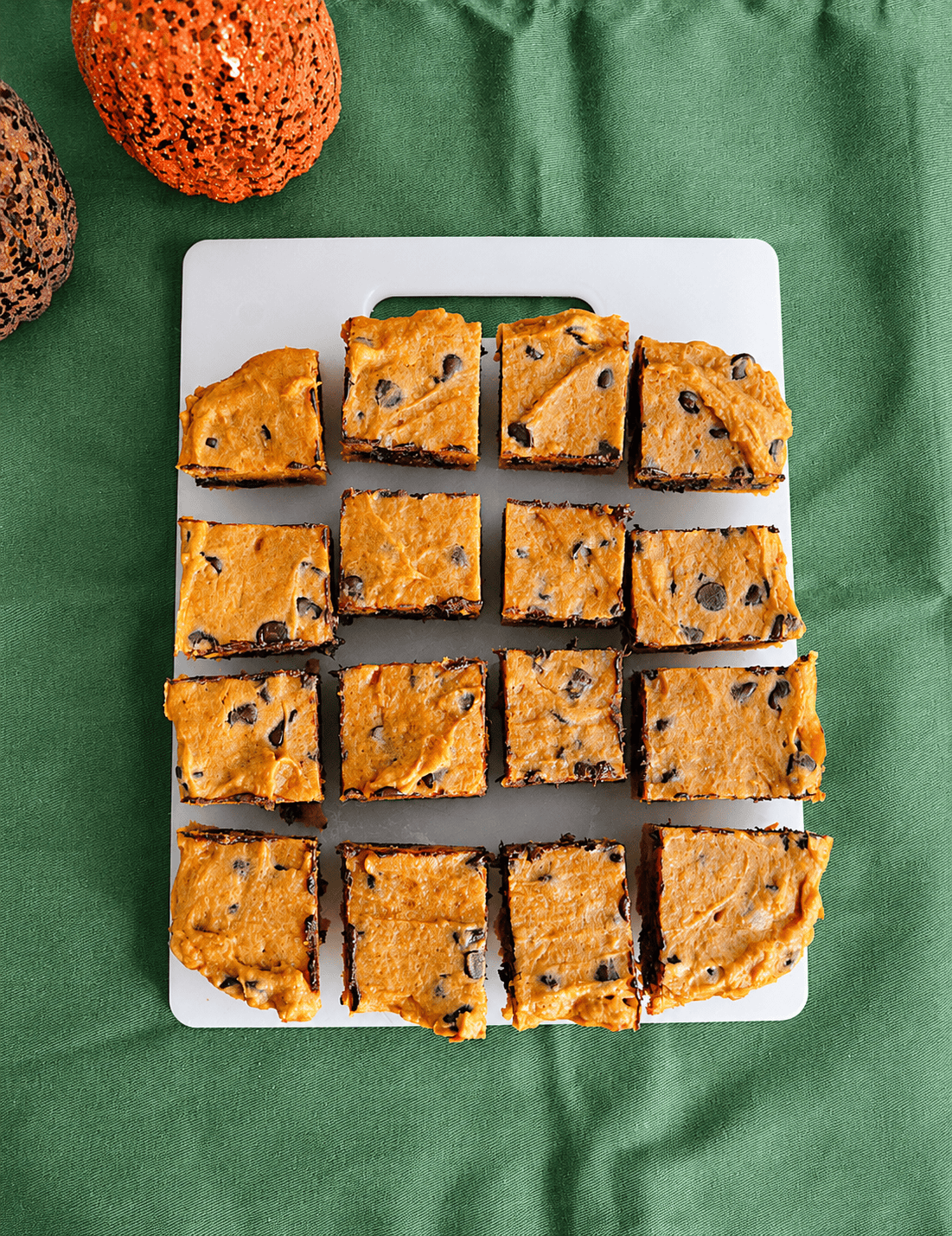 A cutting board with a pan of pumpkin bars cut into 16 pieces.