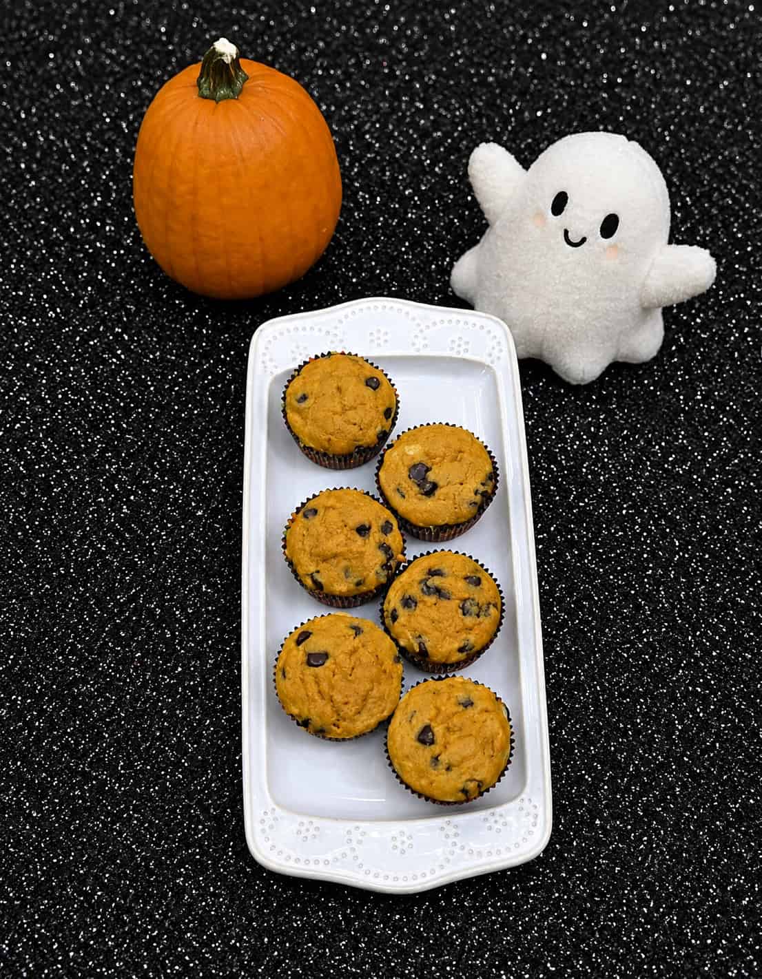 A plate of pumpkin muffins with a ghost and a pumpkin in the background.