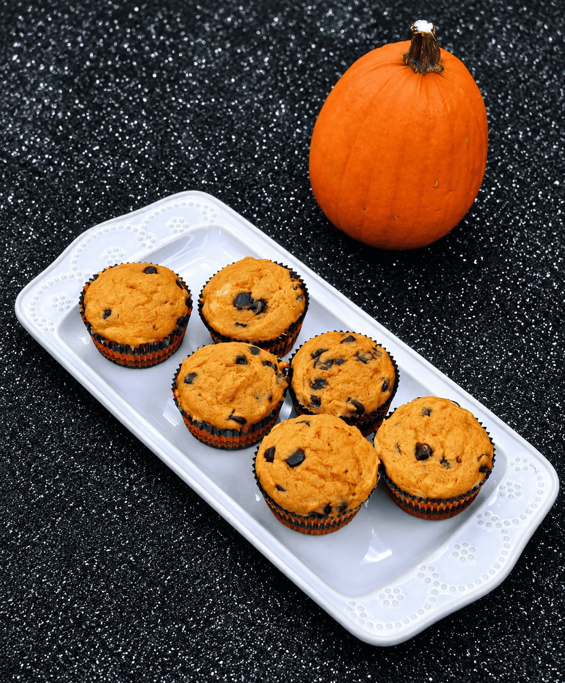 A platter of pumpkin muffins and a pumpkin behind the plate.