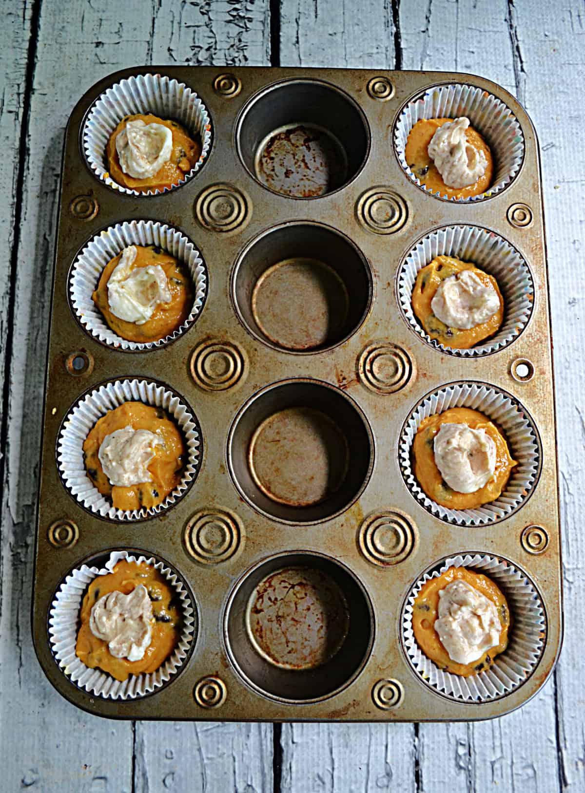 A muffin tin with pumpkin batter and cheesecake in it.