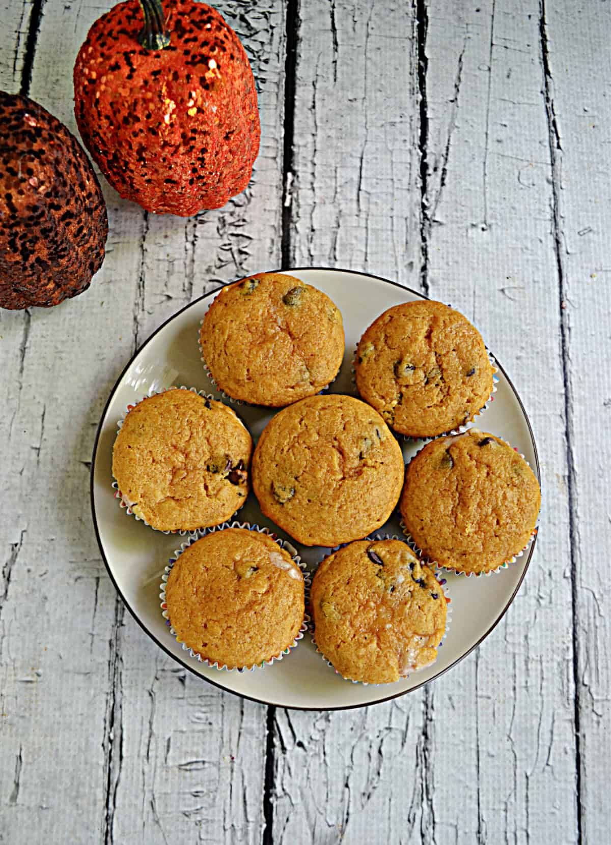 A plate with pumpkin muffins on it and 2 pumpkins behind the plate.