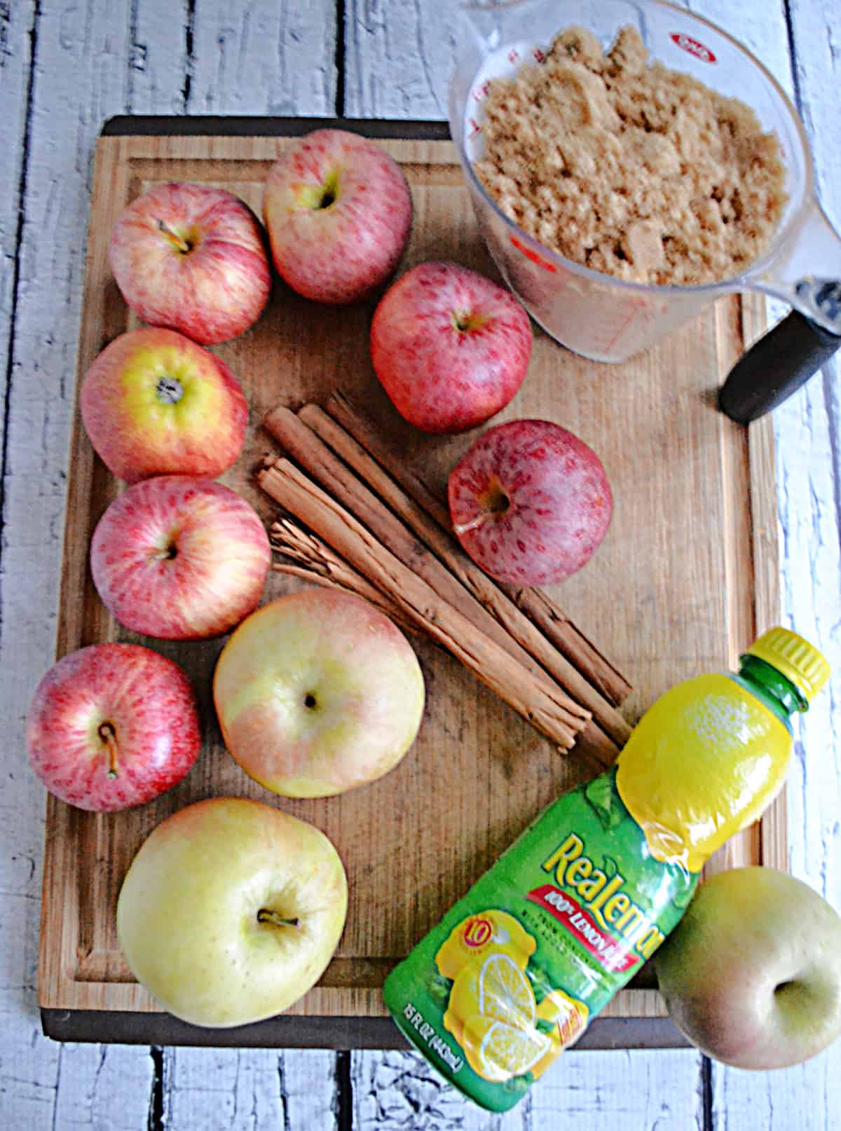 A cutting board with brown sugar, apples, spices, and lemon juice.