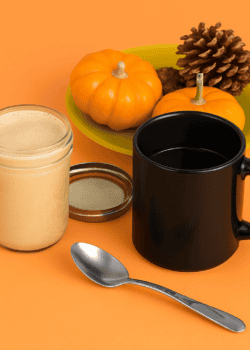 A jar of pumpkin spice creamer, a mug, a spoon, a plate with mini pumpkins on it.