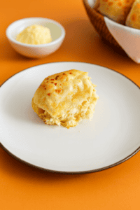 A plate with a roll on it, a bowl of rolls in the background along with a bowl of butter.