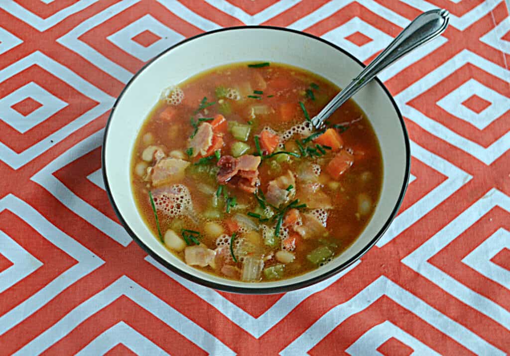 A bowl with beans, bacon, and vegetables in a soup brother with a spoon sticking out of it. 