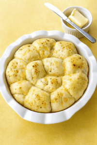 A pan of dinner rolls with a small bowl of butter and a butter knife.