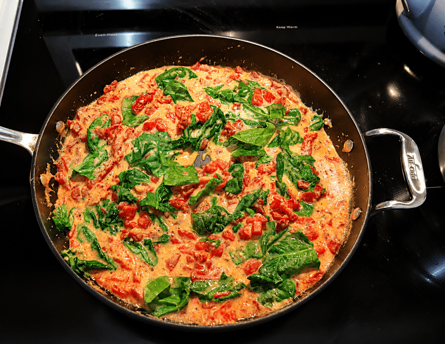 A pan of pasta, tomatoes, and spinach on a stove.