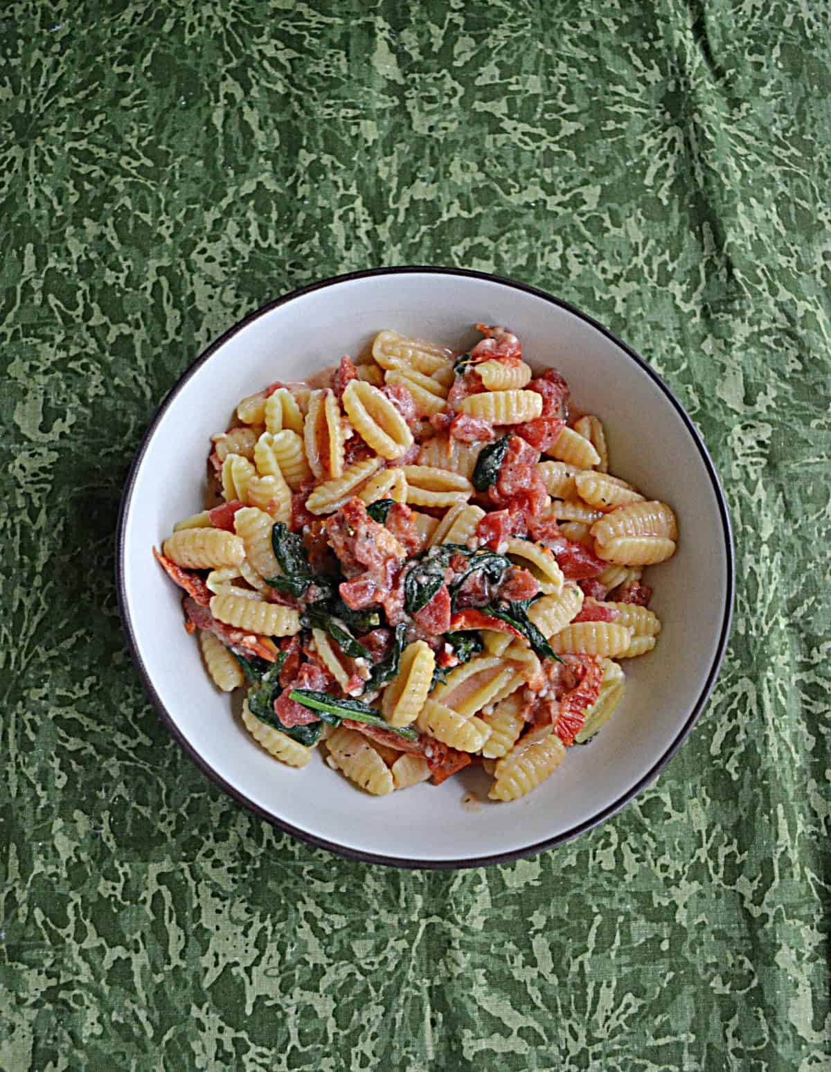 A bowl of pasta with spinach and tomatoes.