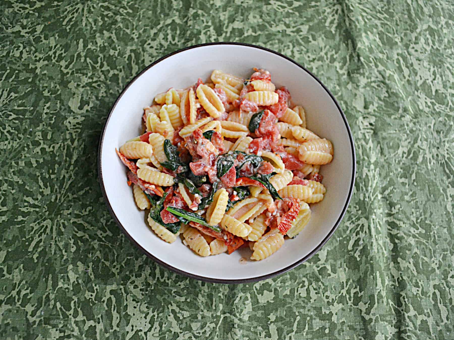 A bowl of pasta with sauce, tomatoes, and spinach.