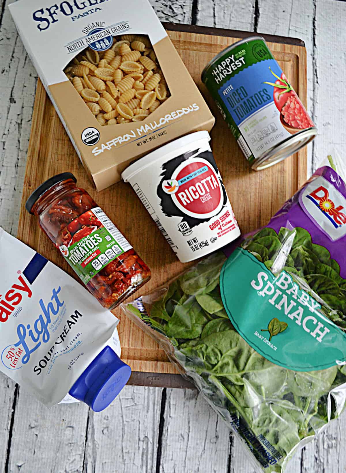 A cutting board with pasta, sauce, ricotta cheese, spinach, tomatoes, and sour cream on it.