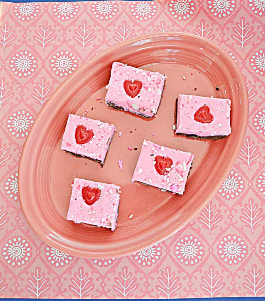 A pink platter with five pieces of Double Layer Double Fudge with milk chocolate on the bottom and pink white chocolate on the top each one with a heart on it on a pink background.